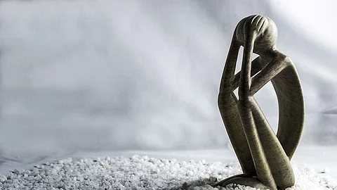 Figur, die in hockender Haltung mit den Händen über dem Gesicht dasitzt.