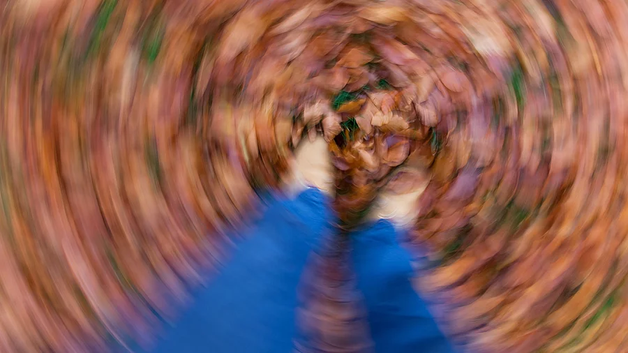 Symbolbild Schwindel: Frau steht in Herbstlaub, alles dreht sich 