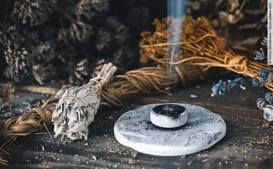 Rauchender Räucherstein neben trockenen Kräutern