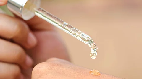Frauenhände auf die mit einer Pipette ein Tropfen Serum aufgetragen wird.