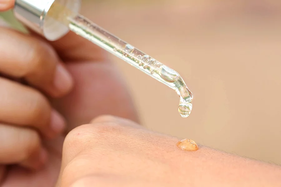 Frauenhände auf die mit einer Pipette ein Tropfen Serum aufgetragen wird.