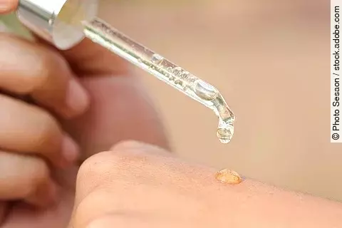 Frauenhände auf die mit einer Pipette ein Tropfen Serum aufgetragen wird.