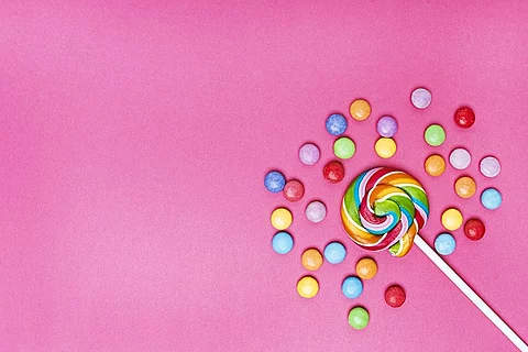 Lutscher in der unteren rechten Ecke umgeben von bunten Bonbons auf rosa Hintergrund.