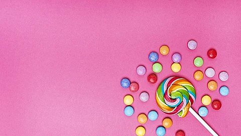 Lutscher in der unteren rechten Ecke umgeben von bunten Bonbons auf rosa Hintergrund.
