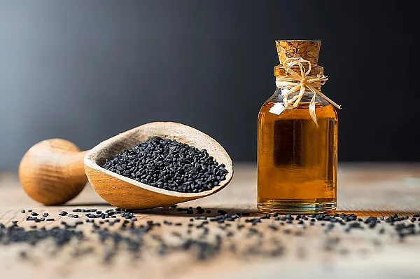 glass bottle of black cumin seeds essential oil , Nigella Sativa Glasflasche mit Schwarzkümmelöl, Holzlöffel mit Schwarkümmelsamen