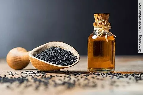Glasflasche mit Schwarzkümmelöl, Holzlöffel mit Schwarkümmelsamen