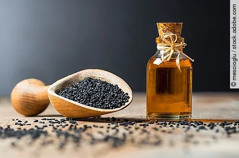 Glasflasche mit Schwarzkümmelöl, Holzlöffel mit Schwarkümmelsamen