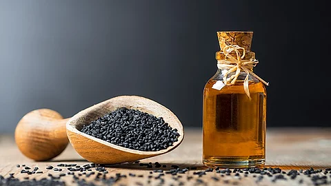 Glasflasche mit Schwarzkümmelöl, Holzlöffel mit Schwarkümmelsamen