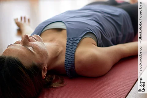 Frau liegt auf Yogamatte, praktiziert Tiefenentspannung