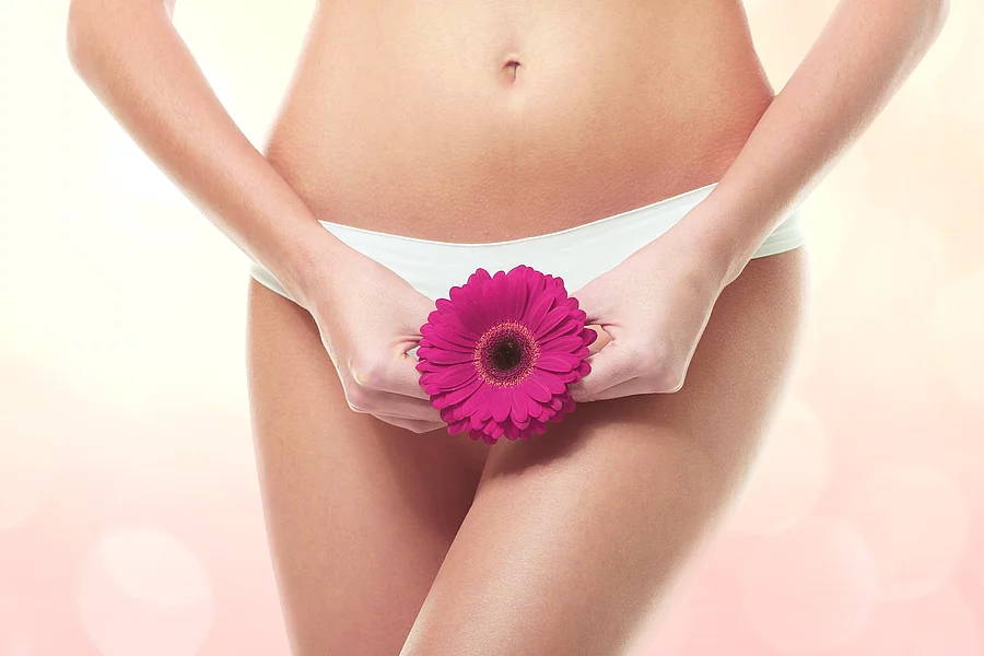Eine junge Frau hält eine lila Blüte vor den Intimbereich