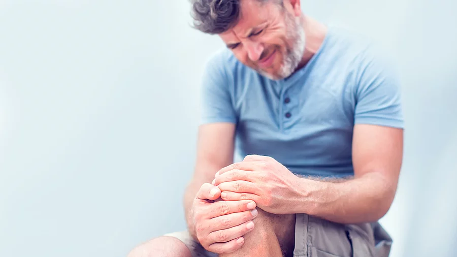 Ein Mann hält mit den Händen sein linkes, schmerzendes Knie fest Ein Mann hält mit den Händen sein linkes, schmerzendes Knie fest