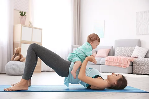 Junge Mutter macht Yoga mit Baby auf dem Bauch liegend