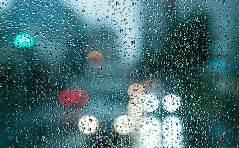 Trüber Herbsttag, durch eine Fensterscheibe mit Regentropfen sieht man Autolichter auf einer Straße und im Hintergrund verschwommene Häuserkonturen