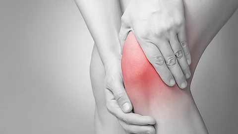 Schwarz-weiß Bild einer Person, die ihr schmerzendes Knie massiert.