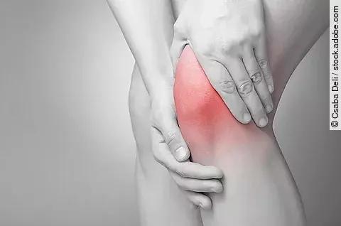 Schwarz-weiß Bild einer Person, die ihr schmerzendes Knie massiert.