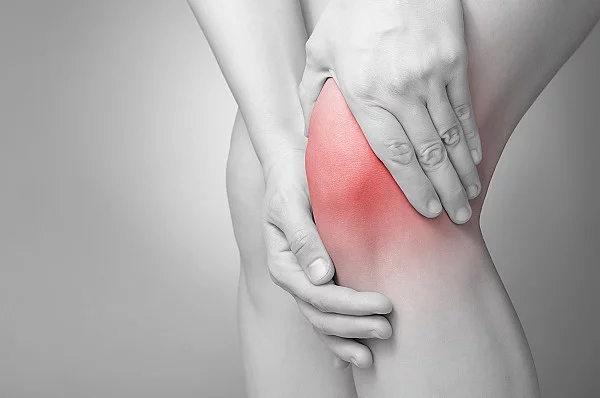 Schwarz-weiß Bild einer Person, die ihr schmerzendes Knie massiert.