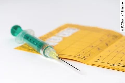 Eine grüne Spritze liegt auf einem aufgeschlagenen Impfpass.