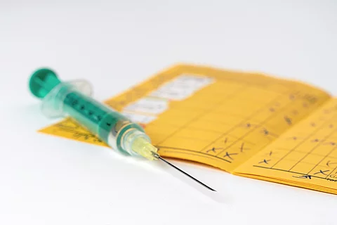 Eine grüne Spritze liegt auf einem aufgeschlagenen Impfpass.