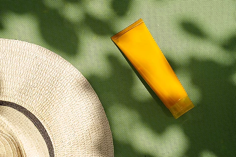 Sonnencremetube und Sonnenhut auf grüner Unterlage