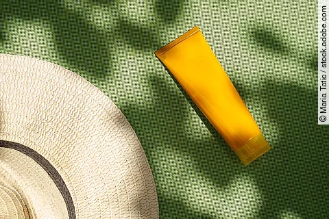Sonnencremetube und Sonnenhut auf grüner Unterlage