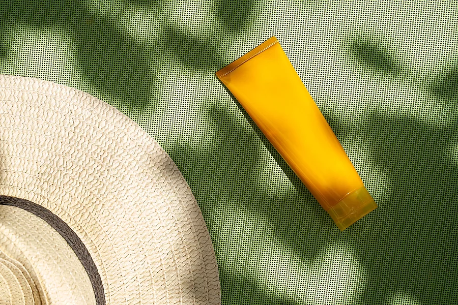 Sonnencremetube und Sonnenhut auf grüner Unterlage