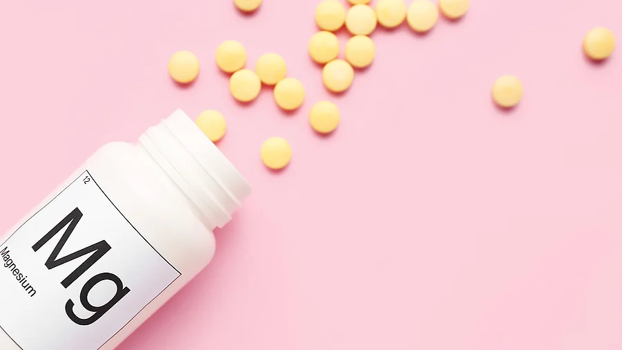 Magnesium-Pillen weißes Fläschchen mit gelben Magnesiumpillen auf rosa Hintergrund
