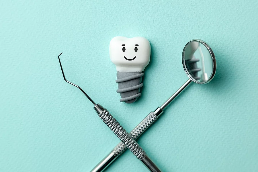 Zahn mit Implantat und Smiley, Zahnarztbesteck auf türkisem Hintergrund