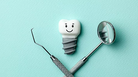 Zahn mit Implantat und Smiley, Zahnarztbesteck auf türkisem Hintergrund