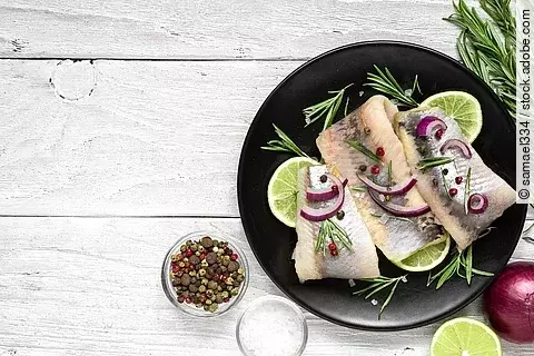 Hering mit Pfeffer, Rosmarin und roter Zwiebel auf schwarzem Teller