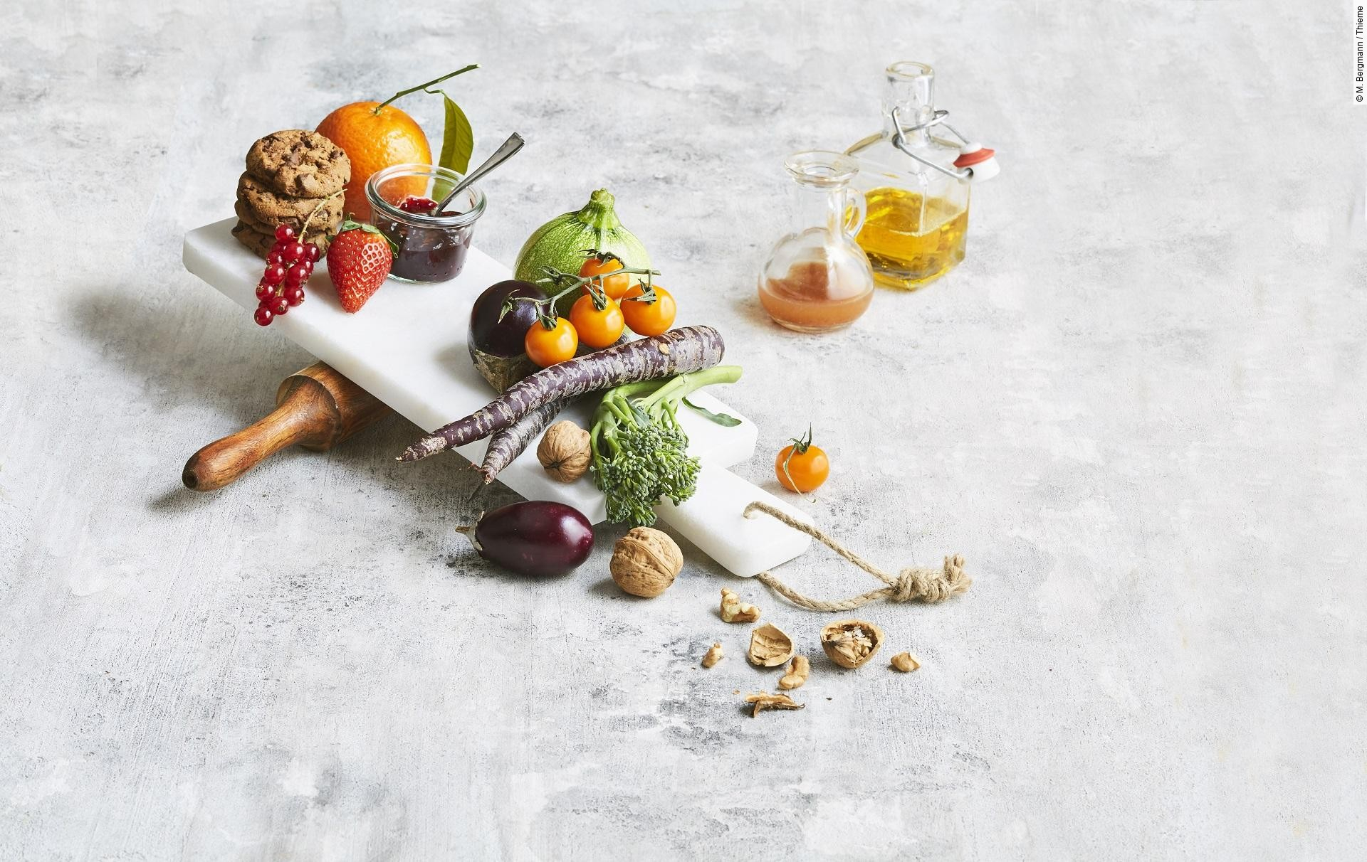 Obst, Gemüse, Marmelade, Nüsse, Cookies, Öl und Saft ästhetisch gruppiert auf weißem Untergrund