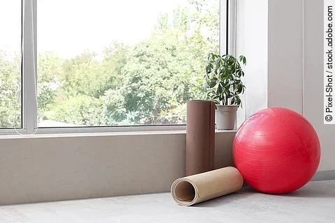 Gymnastikball und 2 Fitnessmatten neben einem Fenster