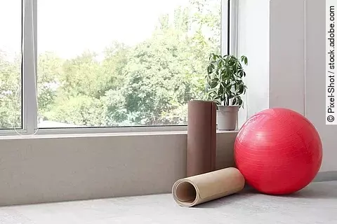 Gymnastikball und 2 Fitnessmatten neben einem Fenster