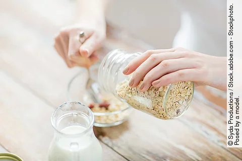 Ein Frau schüttet Haferflocken in eine Schüssel