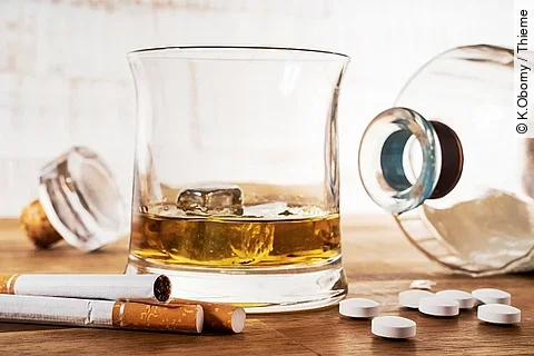 Zigaretten, Tabletten, eine liegende Glasflasche und ein Glas mit Whiskey sind auf einem Holztisch ausgebreitet.