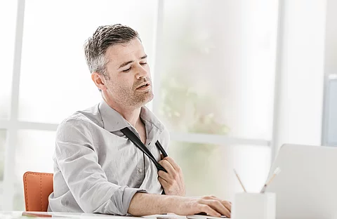 Büroarbeiter lockert angestrengt seinen Schlips, es ist heiß