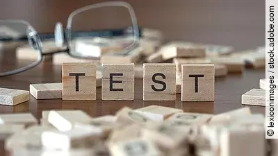 4 Holzklötzchen mit den Buchstaben TEST, dahinter liegt eine Brille