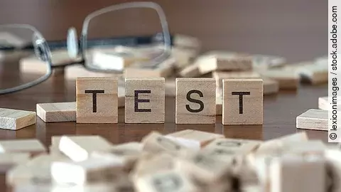 4 Holzklötzchen mit den Buchstaben TEST, dahinter liegt eine Brille