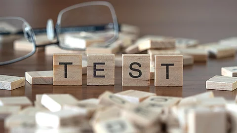 4 Holzklötzchen mit den Buchstaben TEST, dahinter liegt eine Brille