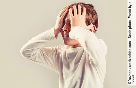 Kind mit Migräne hält sich mit schmerzverzerrtem Gesicht den Kopf.