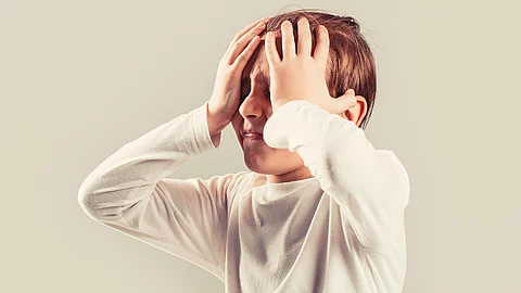 Kind mit Migräne hält sich mit schmerzverzerrtem Gesicht den Kopf.
