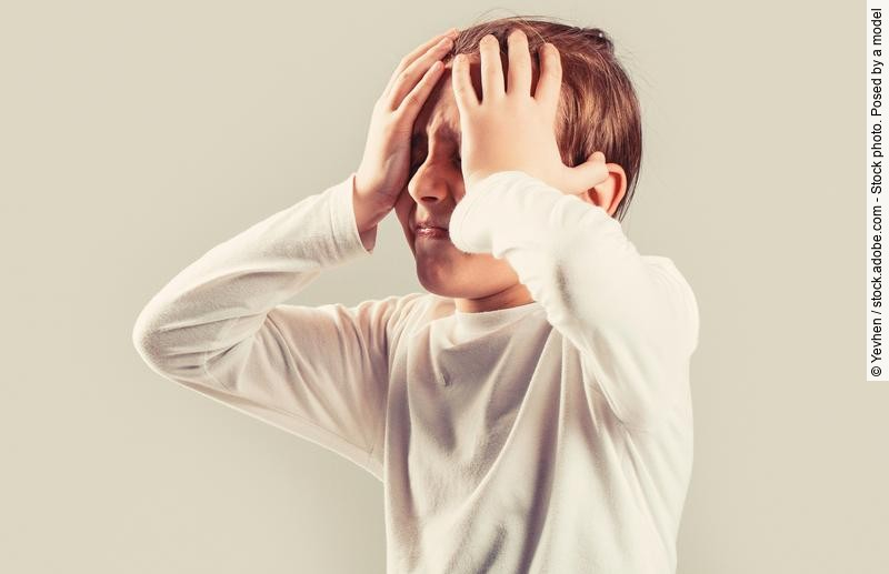 Kind mit Migräne hält sich mit schmerzverzerrtem Gesicht den Kopf.