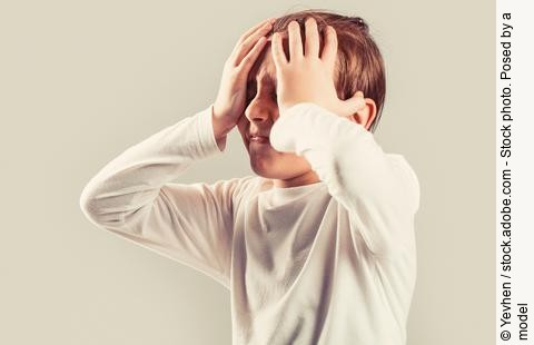 Kind mit Migräne hält sich mit schmerzverzerrtem Gesicht den Kopf.