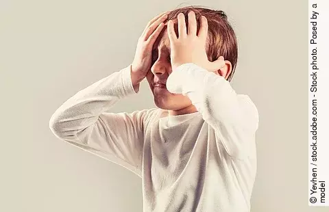 Kind mit Migräne hält sich mit schmerzverzerrtem Gesicht den Kopf.