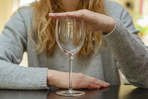 Frau sitzt am Tisch und hält leeres Weinglas zu