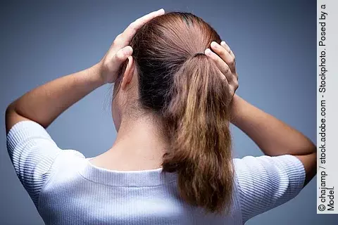 Frau mit Kopfschmerzen hält sich den Hinterkopf