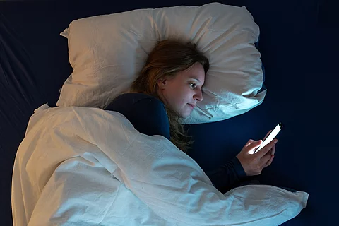 Jugendliche liegt im Bett und liest auf dem Smartphone