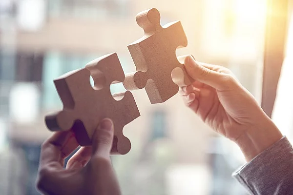 Woman hand connecting jigsaw puzzle on desk, Business solutions, Zwei Hände, die zwei Puzzelstücke aneinander halten.