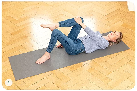 Junge Frau in Alltagskleidung macht Übungen auf Yogamatte 