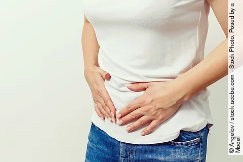 Frau in Jeans und weißem T-Shirt hält sich den Bauch