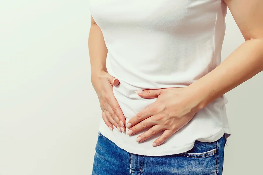 Frau in Jeans und weißem T-Shirt hält sich den Bauch